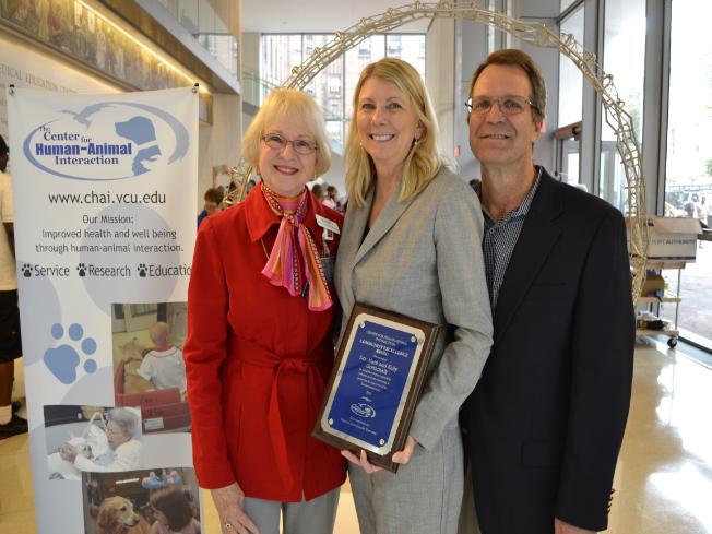 Drs. Mark and Kelly Gottschalk stand with Dr. Sandra Barker after accepting the Community Excellence Award (a blue plaque thanking them for their support) at the 2016 Pups on the Plaza